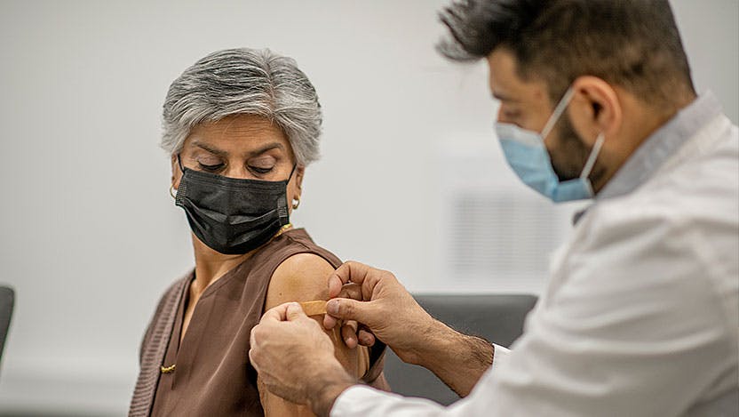 Masked nurse places bandaid on masked patient's arm after vaccination