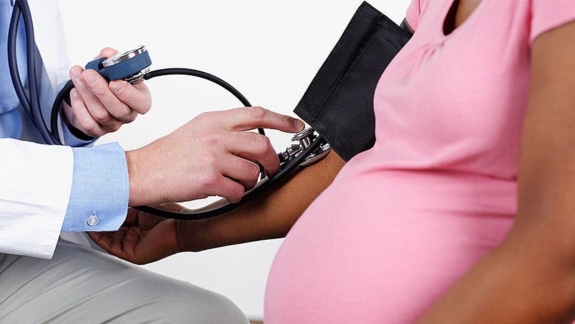 Doctor using blood pressure cuff of pregnant patient