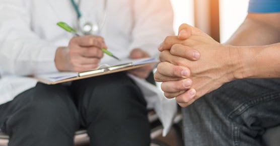 Male patient clasping hands, doctor taking notes