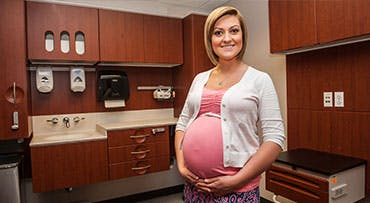 Pregnant woman smiling and holding her belly in Family BIrth Center exam room